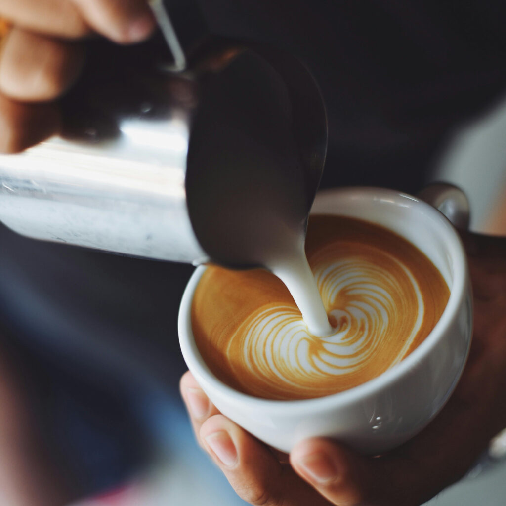 Barista gießt Milch in den Kaffee ein