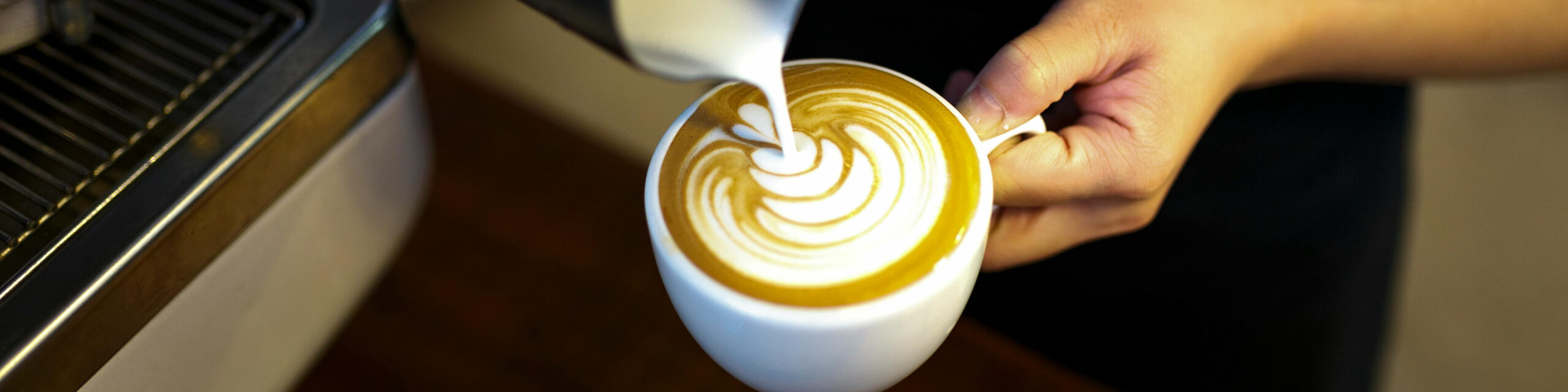 Barista gießt Milch in den Kaffee ein